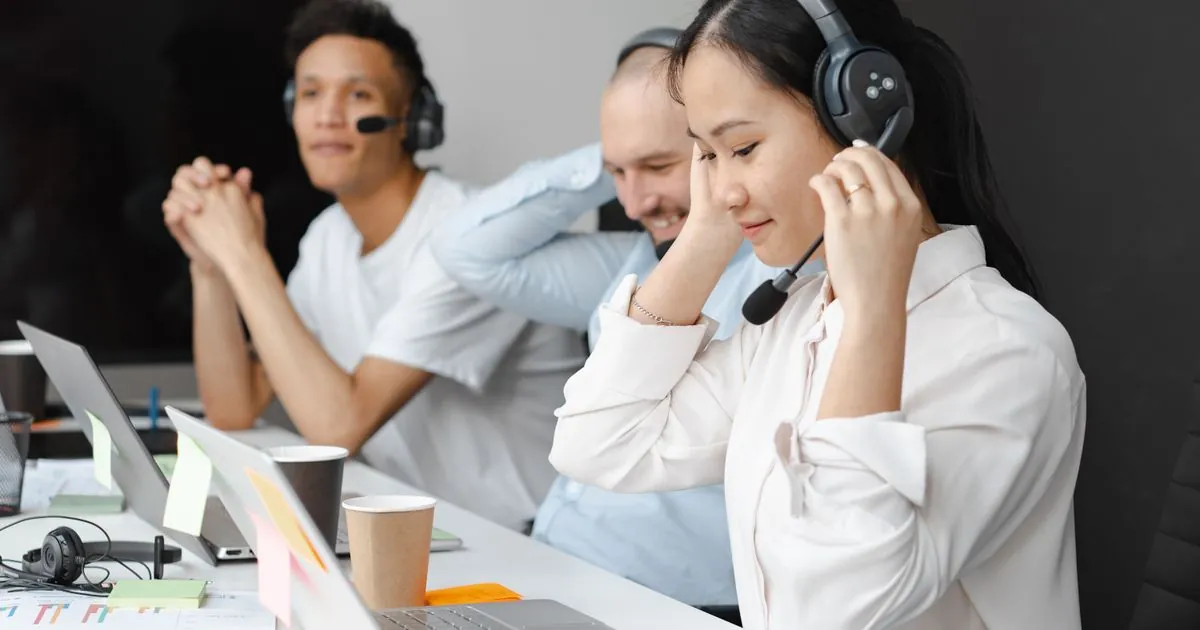 A diverse team of call center agents wearing headsets work at laptops in a modern office